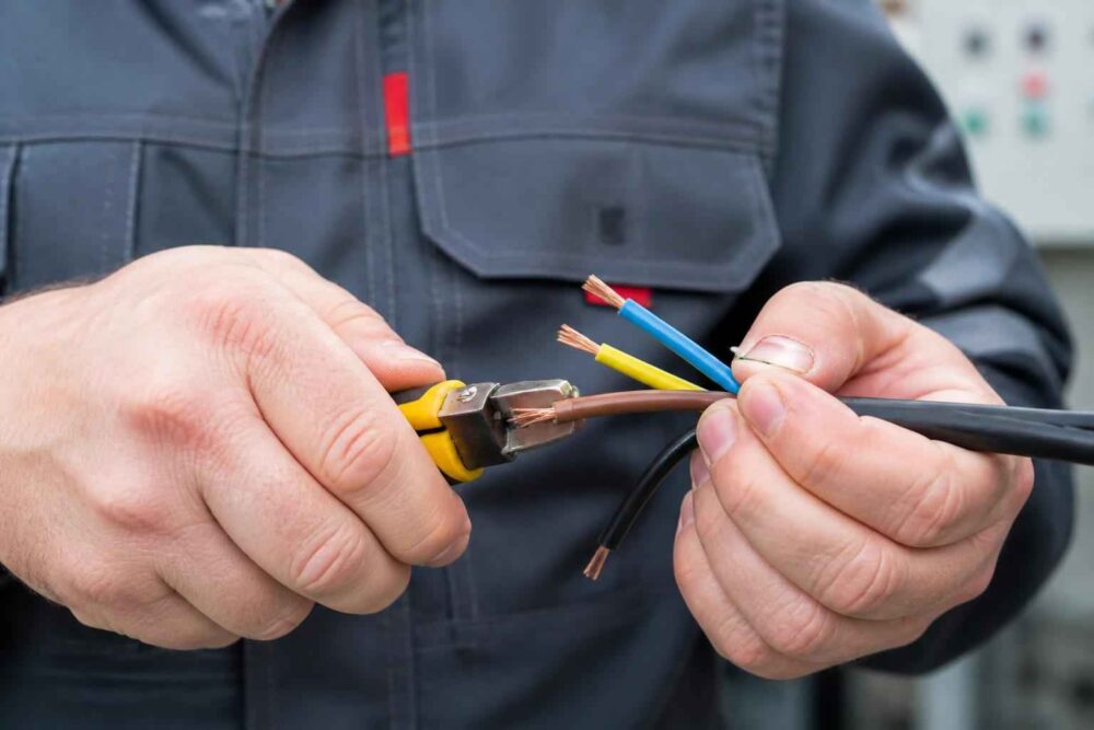Elektryk w rękawicach łączy kolorowe przewody za pomocą narzędzia zaciskowego