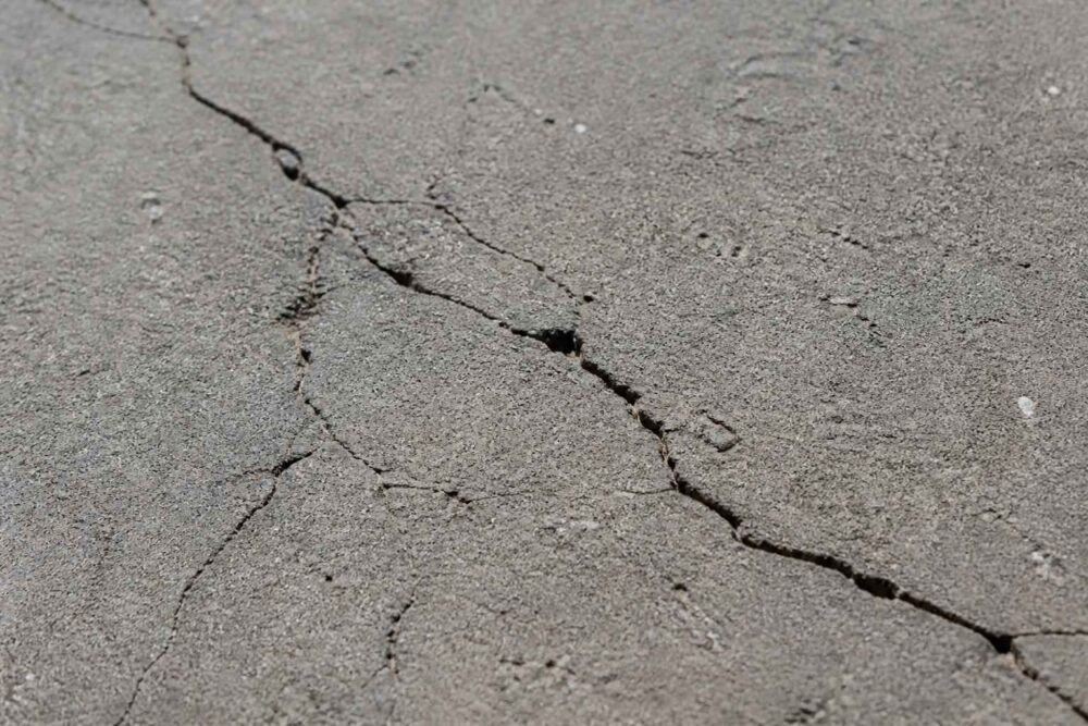 Zbliżenie na rozległe pęknięcia w szarej nawierzchni asfaltowej