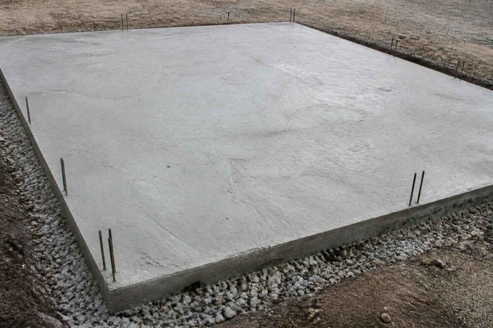 Gładka betonowa płyta na żwirowym podłożu z wystającymi prętami zbrojeniowymi przy krawędziach
