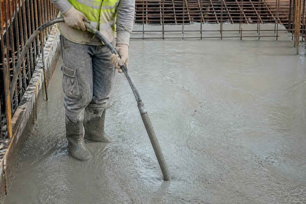Pracownik wyrównuje świeży beton za pomocą wibratora na placu budowy